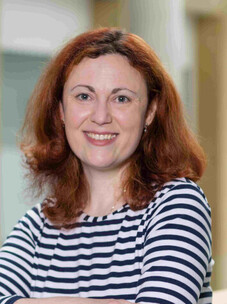 Anna Isaeva mit rotbraunem Haar, gestreiftem Oberteil und freundlichem Lächeln.